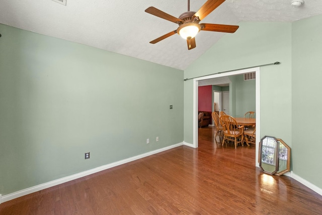 unfurnished room featuring a textured ceiling, lofted ceiling, wood finished floors, visible vents, and baseboards