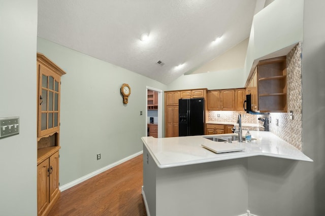 kitchen with a peninsula, vaulted ceiling, light wood-type flooring, black appliances, and a sink