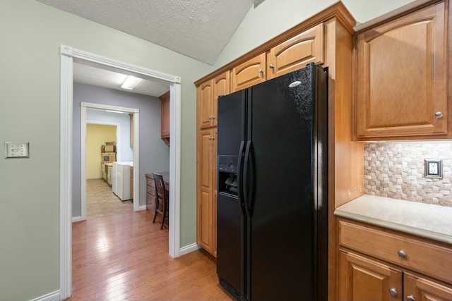 kitchen featuring light wood finished floors, backsplash, a textured ceiling, baseboards, and black fridge