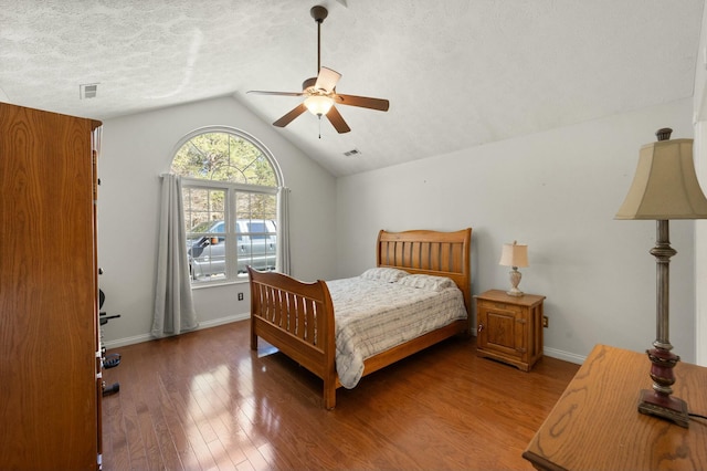 bedroom featuring baseboards, visible vents, wood finished floors, vaulted ceiling, and a textured ceiling