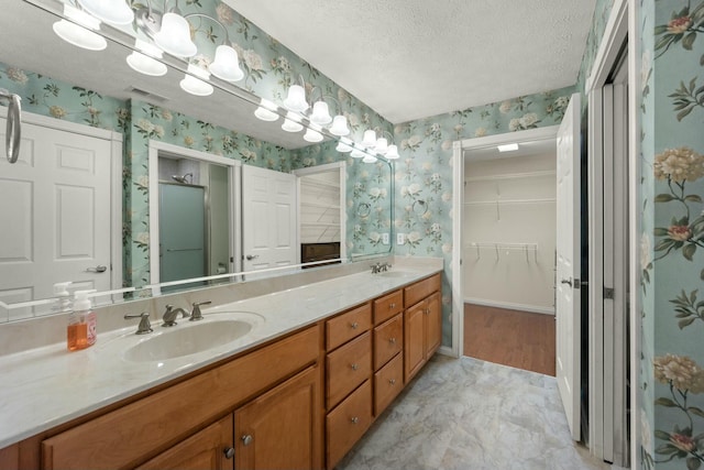 full bathroom with a textured ceiling, a sink, and wallpapered walls