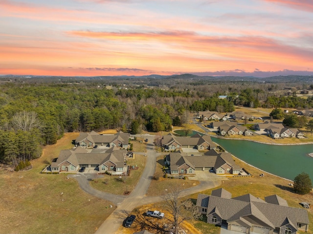 aerial view at dusk featuring a water view, a residential view, and a view of trees