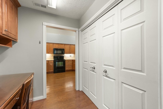 hallway featuring a textured ceiling, visible vents, and light wood-style floors