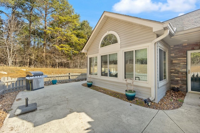 view of side of property with a patio, roof with shingles, stone siding, and fence