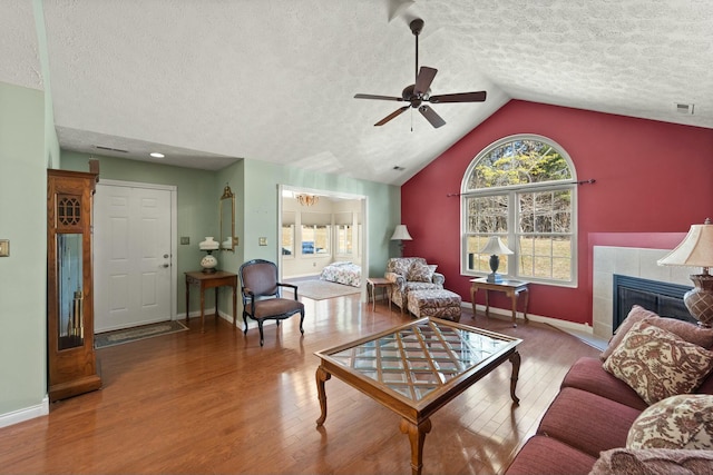 living room with vaulted ceiling, a tiled fireplace, wood finished floors, and visible vents