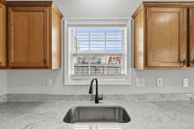 kitchen with light stone counters, brown cabinets, and a sink