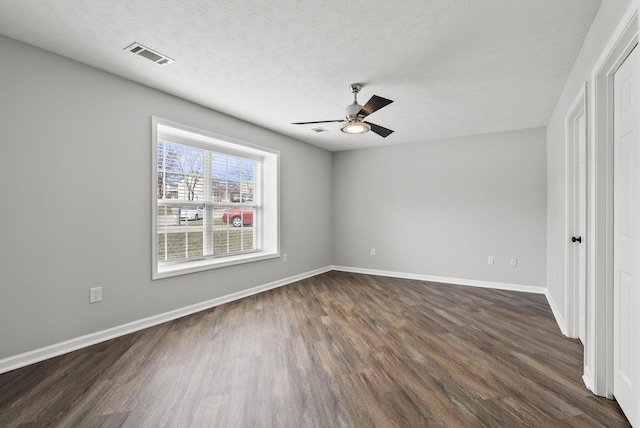 unfurnished room with a textured ceiling, a ceiling fan, visible vents, baseboards, and dark wood finished floors