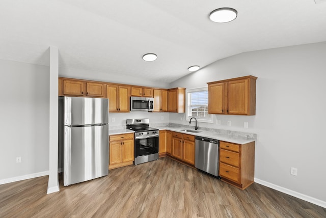 kitchen featuring stainless steel appliances, wood finished floors, a sink, vaulted ceiling, and light countertops