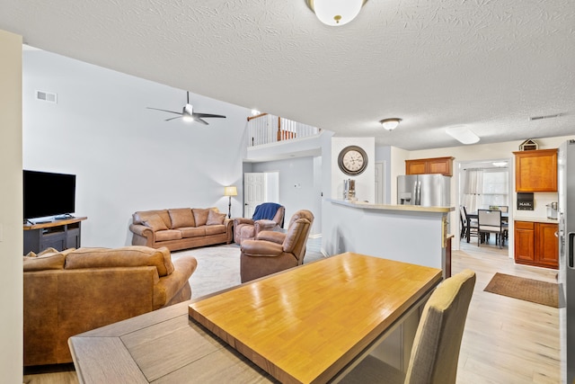 dining space featuring a textured ceiling, light wood-style flooring, visible vents, and a ceiling fan