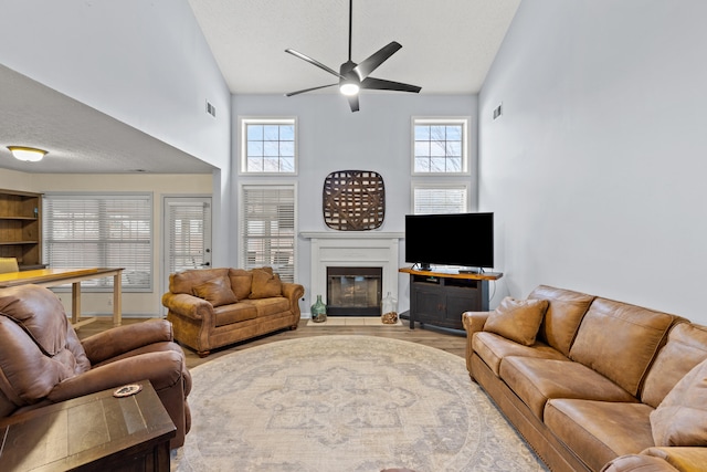 living area featuring high vaulted ceiling, wood finished floors, plenty of natural light, and a glass covered fireplace