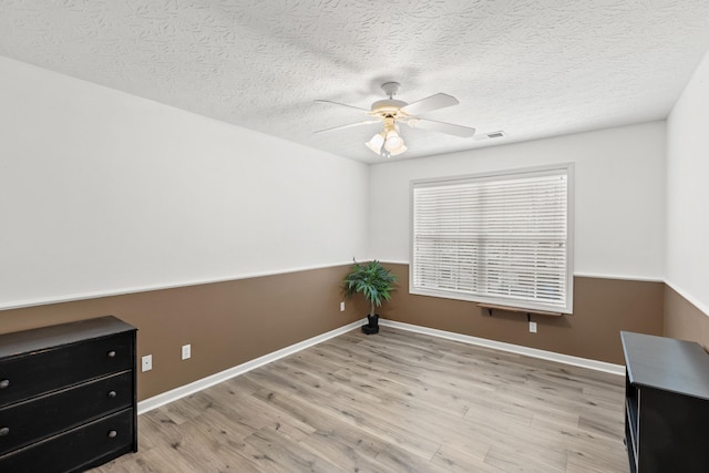 unfurnished office with ceiling fan, a textured ceiling, wood finished floors, visible vents, and baseboards