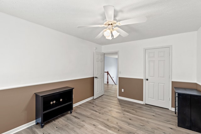 bedroom with a textured ceiling, light wood-type flooring, a ceiling fan, and baseboards