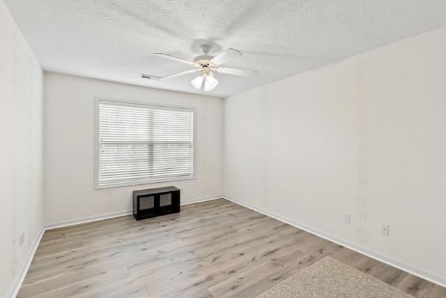 spare room with light wood-type flooring, visible vents, ceiling fan, and a textured ceiling