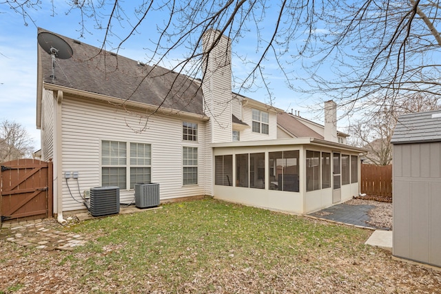 back of property featuring a chimney, a lawn, a sunroom, a gate, and a fenced backyard