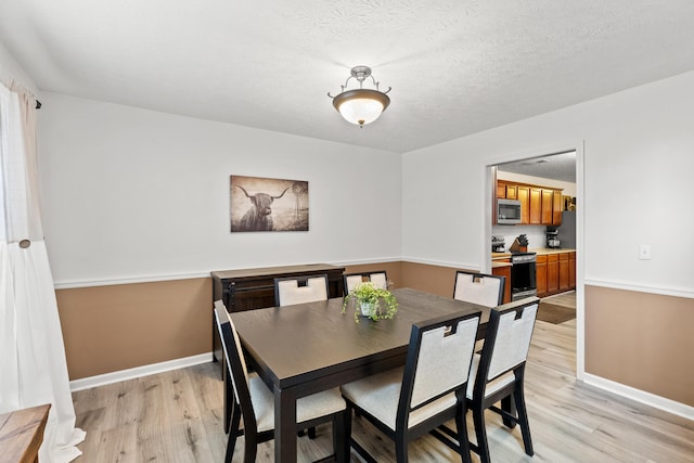 dining room featuring a textured ceiling, baseboards, and light wood-style floors