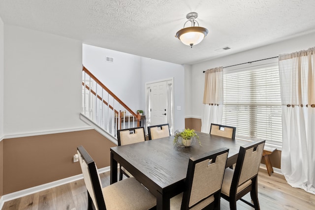 dining room featuring visible vents, light wood-style flooring, baseboards, and stairs