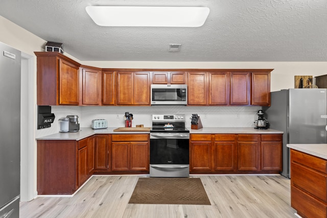 kitchen featuring stainless steel appliances, light countertops, light wood-style flooring, and a textured ceiling