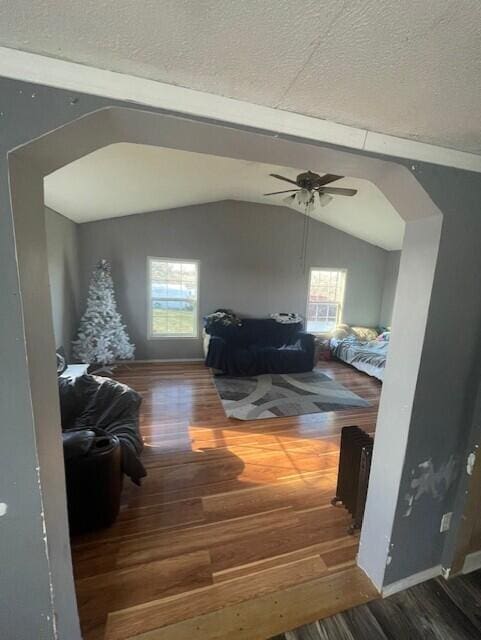 interior space with arched walkways, ceiling fan, vaulted ceiling, a textured ceiling, and wood finished floors