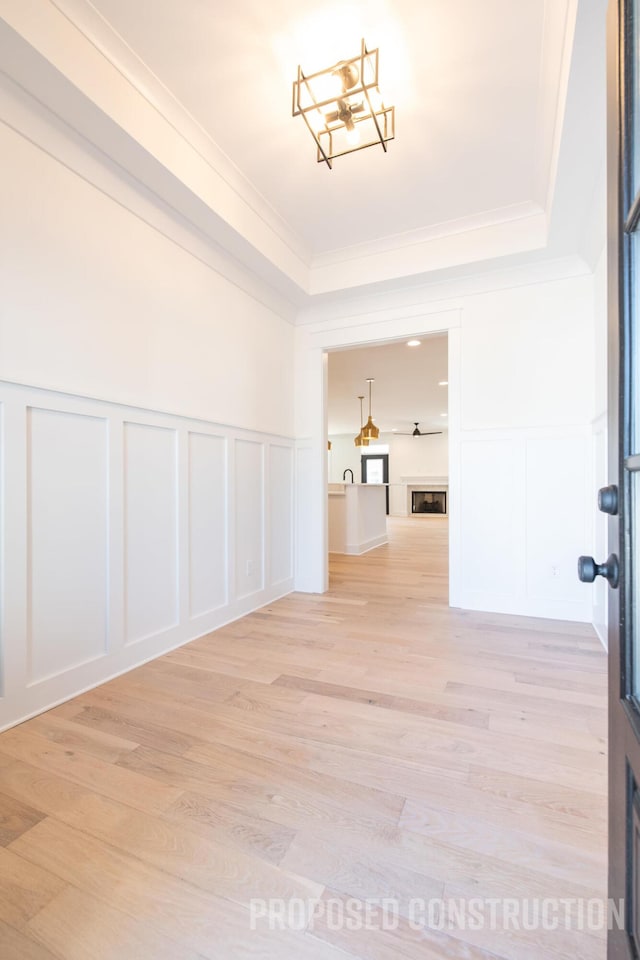 spare room featuring ornamental molding, a fireplace, a decorative wall, and light wood finished floors