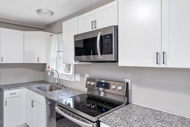 kitchen with stainless steel appliances, a sink, white cabinetry, and light stone countertops