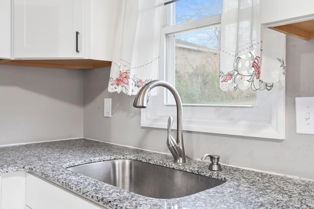 details featuring a sink, light stone countertops, and white cabinets