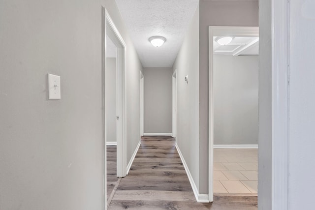 hallway featuring baseboards, a textured ceiling, and wood finished floors