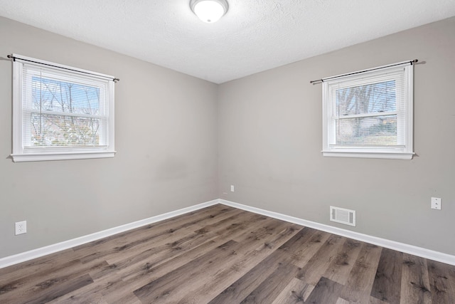 unfurnished room with visible vents, a textured ceiling, baseboards, and wood finished floors