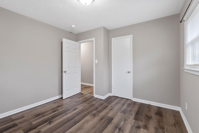 unfurnished bedroom featuring a textured ceiling, a closet, wood finished floors, and baseboards