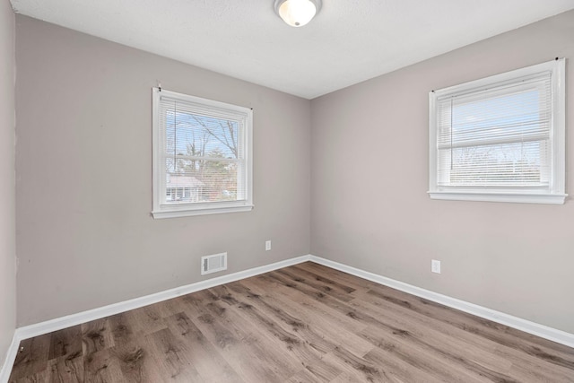 unfurnished room featuring baseboards, visible vents, and wood finished floors