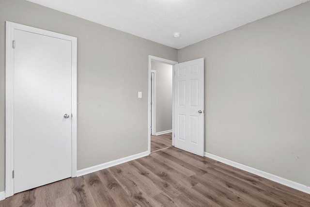 unfurnished bedroom with a textured ceiling, baseboards, and wood finished floors