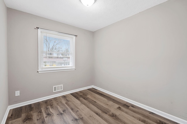 unfurnished room with visible vents, a textured ceiling, baseboards, and wood finished floors