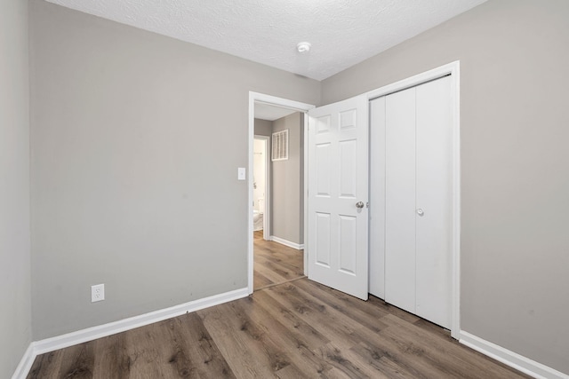 unfurnished bedroom with a textured ceiling, a closet, baseboards, and wood finished floors