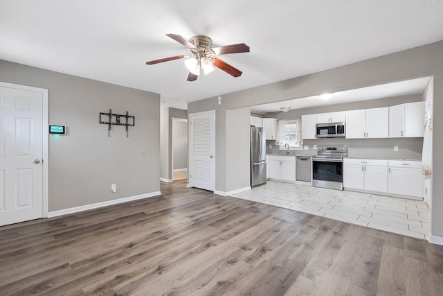 kitchen with light wood finished floors, stainless steel appliances, white cabinetry, a sink, and baseboards