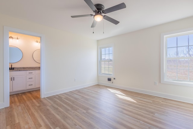 unfurnished bedroom featuring baseboards, a ceiling fan, ensuite bath, light wood-style floors, and a sink