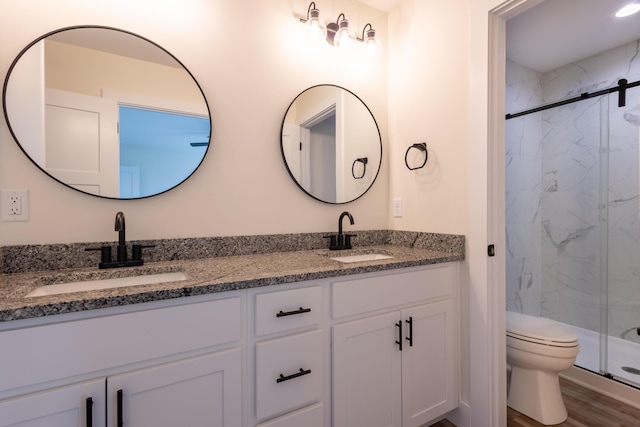 bathroom featuring a marble finish shower, a sink, toilet, and double vanity