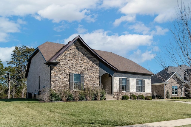 view of front of home with a front yard, cooling unit, roof with shingles, stone siding, and brick siding