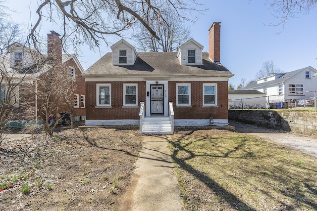 cape cod house with a front yard, fence, brick siding, and a chimney