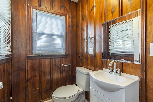 half bath featuring toilet, a healthy amount of sunlight, wood walls, and vanity