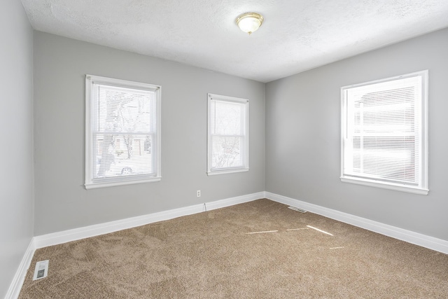 unfurnished room with carpet flooring, baseboards, visible vents, and a textured ceiling