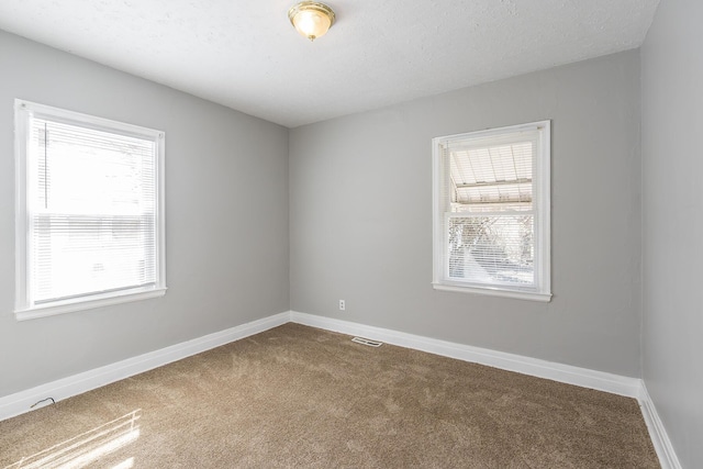 spare room with visible vents, dark carpet, a textured ceiling, and baseboards