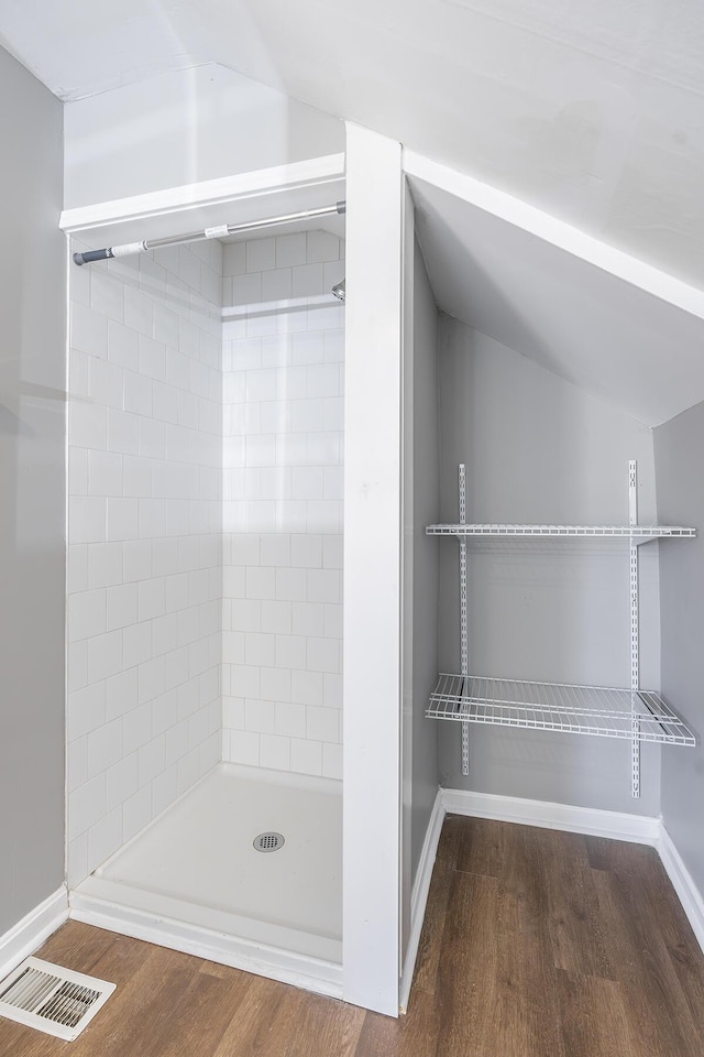 full bath featuring visible vents, wood finished floors, baseboards, a shower stall, and lofted ceiling