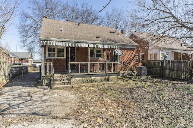 rear view of property featuring brick siding, a porch, a chimney, and fence