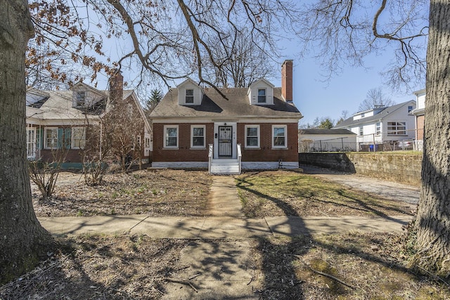 new england style home featuring brick siding, a chimney, and fence