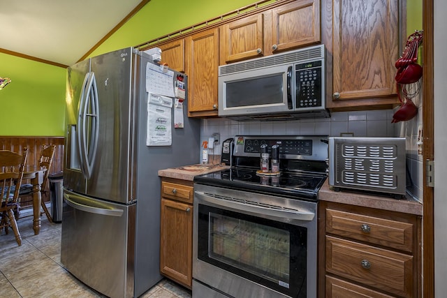 kitchen with lofted ceiling, light tile patterned floors, decorative backsplash, brown cabinets, and stainless steel appliances