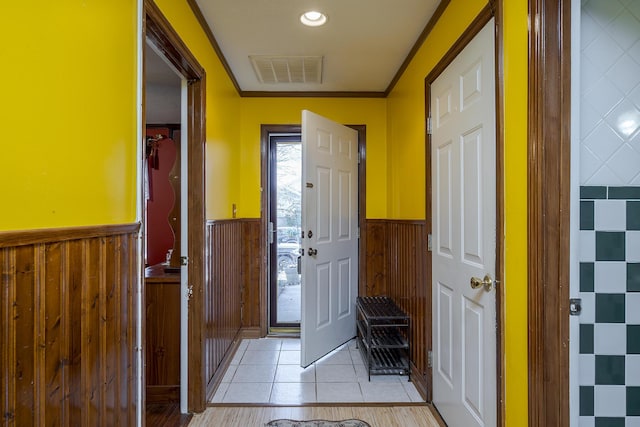 foyer featuring visible vents, wood walls, light tile patterned flooring, wainscoting, and crown molding