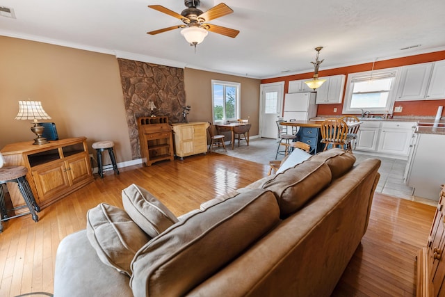 living area with a ceiling fan, ornamental molding, light wood-style flooring, and plenty of natural light