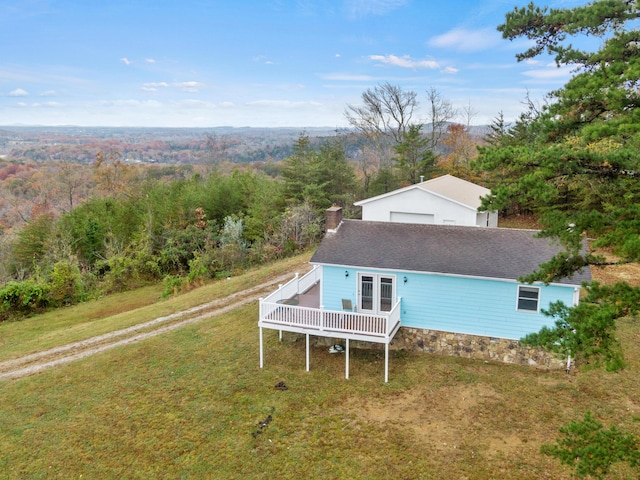 back of house with a deck, a forest view, a chimney, and roof with shingles