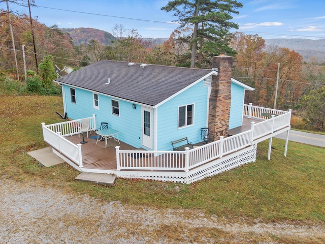 rear view of property featuring a lawn, roof with shingles, a deck with mountain view, and a chimney