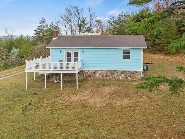 rear view of property with a chimney, a wooden deck, a shingled roof, and a lawn