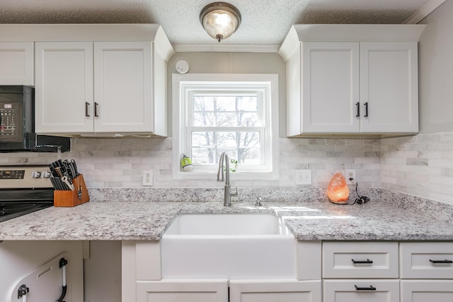 kitchen featuring black microwave, backsplash, a sink, and white cabinets